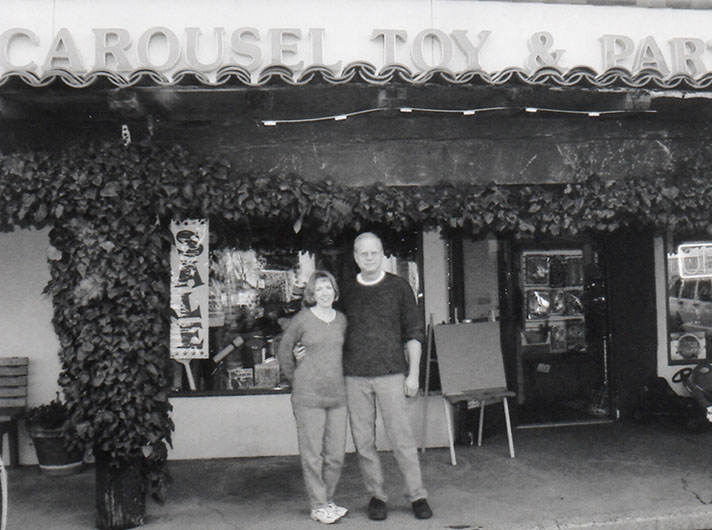 A black and white picture of a woman and man standing in front of Carousel Toy store